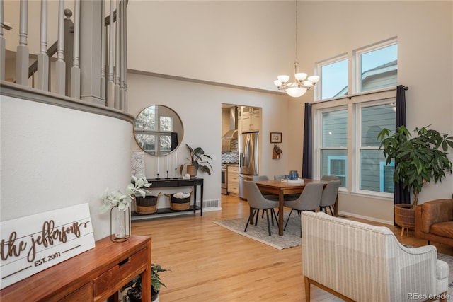 dining area featuring visible vents, a high ceiling, light wood-style flooring, and a notable chandelier