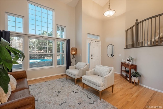 sitting room with light wood finished floors, a high ceiling, and baseboards