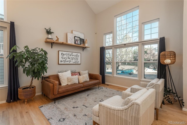 sitting room with light wood-type flooring, high vaulted ceiling, and baseboards