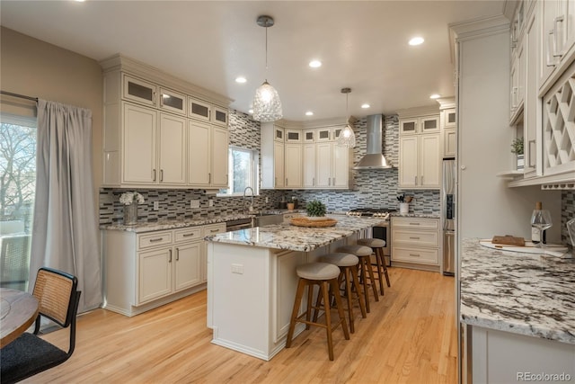 kitchen featuring a center island, stainless steel appliances, backsplash, wall chimney range hood, and a kitchen breakfast bar