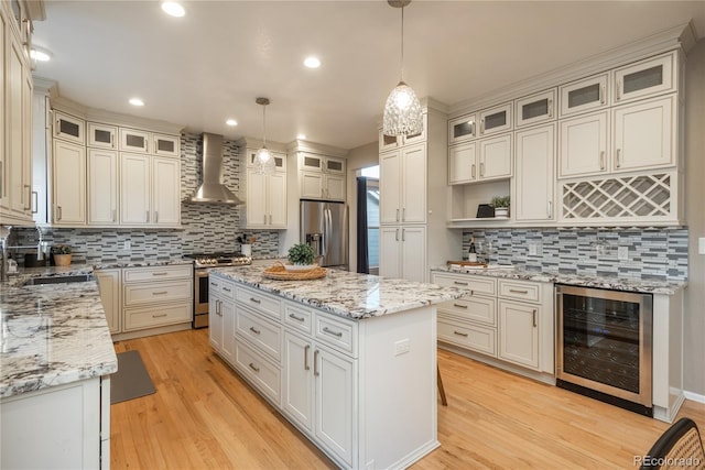 kitchen featuring wine cooler, a center island, appliances with stainless steel finishes, a sink, and wall chimney exhaust hood