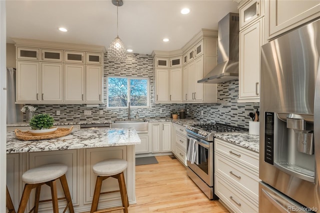 kitchen featuring tasteful backsplash, a kitchen breakfast bar, stainless steel appliances, wall chimney range hood, and a sink