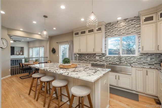 kitchen with a center island, a sink, light wood-type flooring, a kitchen bar, and backsplash