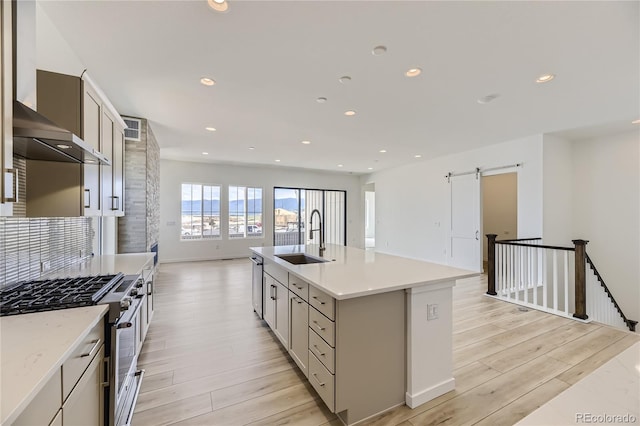 kitchen with appliances with stainless steel finishes, sink, a barn door, wall chimney range hood, and a center island with sink