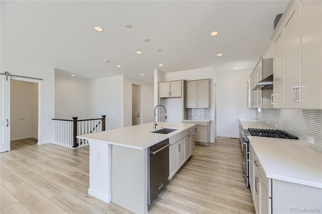 kitchen featuring dishwasher, sink, a barn door, an island with sink, and high end range