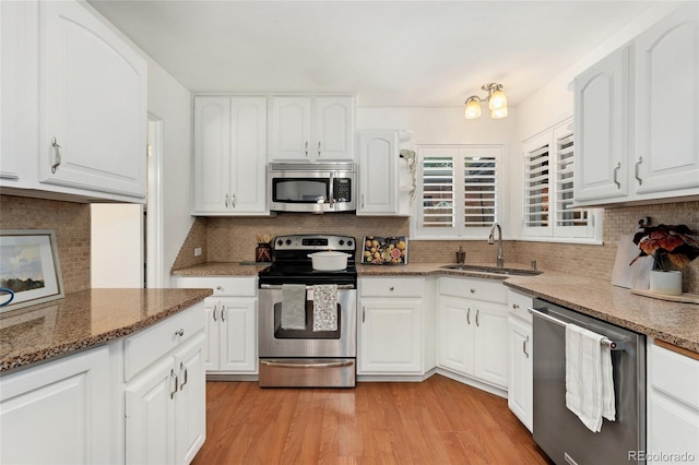 kitchen with light wood-type flooring, dark stone counters, sink, stainless steel appliances, and white cabinetry