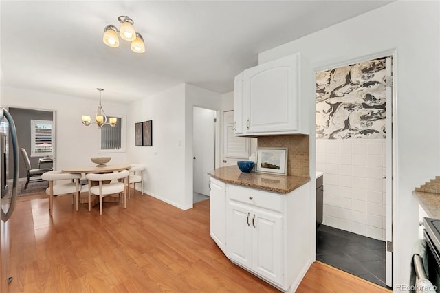 kitchen featuring light wood-type flooring, stove, dark stone countertops, hanging light fixtures, and white cabinets