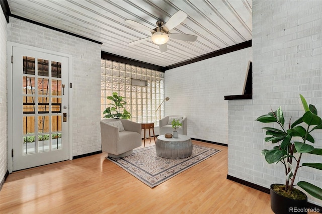 living area featuring ceiling fan, brick wall, hardwood / wood-style floors, and a healthy amount of sunlight