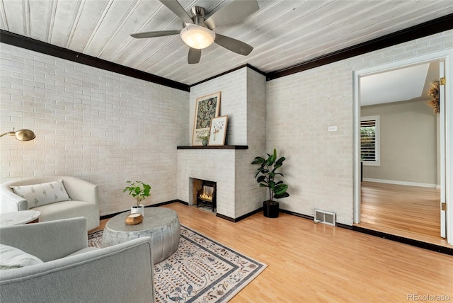 living room featuring ceiling fan, a large fireplace, brick wall, ornamental molding, and hardwood / wood-style flooring