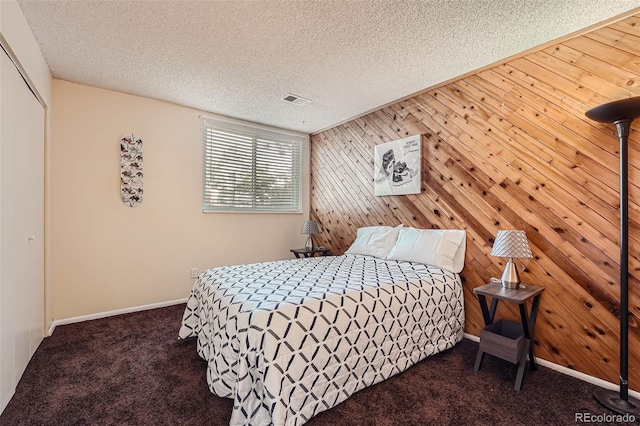 bedroom featuring wood walls, dark carpet, and a textured ceiling