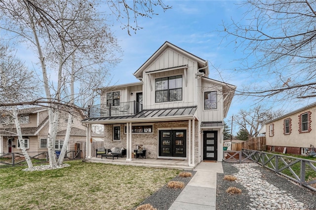 view of front facade featuring board and batten siding, a front yard, a fenced backyard, a balcony, and a standing seam roof