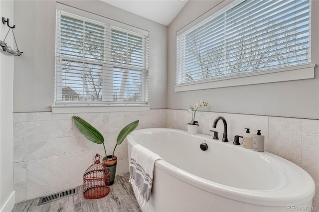 bathroom with tile walls, a bathtub, wood finished floors, and visible vents