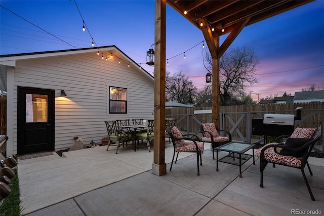 patio terrace at dusk with a fenced backyard, outdoor dining space, and a grill