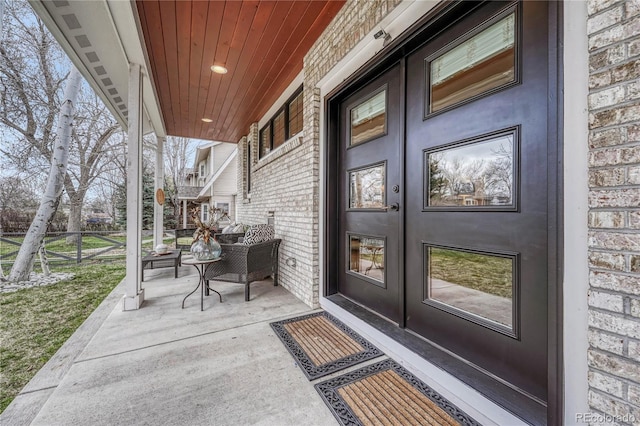 entrance to property featuring brick siding, fence, french doors, and a porch