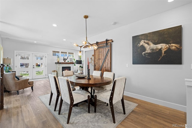 dining area featuring a fireplace, a barn door, wood finished floors, baseboards, and recessed lighting
