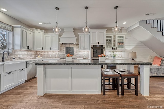 kitchen with custom exhaust hood, a kitchen breakfast bar, a center island, a sink, and stainless steel appliances