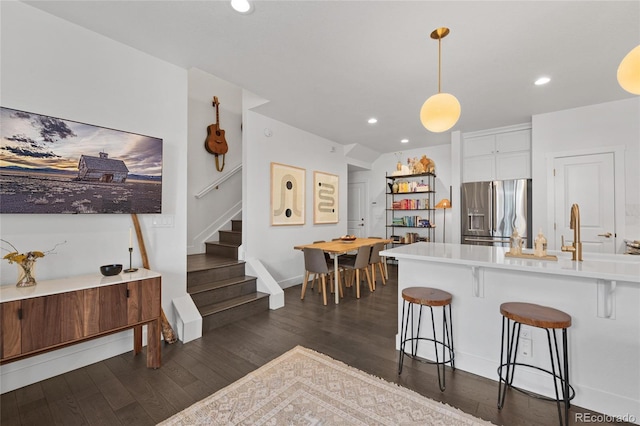 kitchen with dark hardwood / wood-style floors, stainless steel fridge, pendant lighting, a breakfast bar, and white cabinets