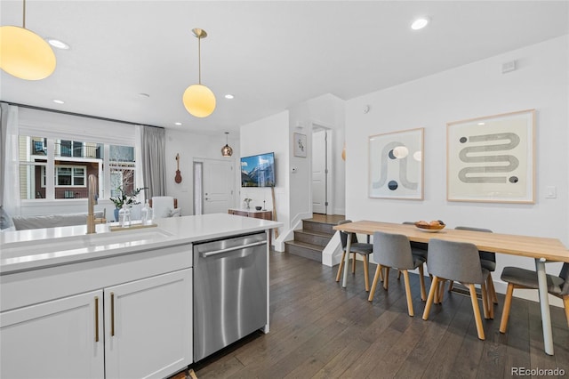 kitchen featuring dark hardwood / wood-style flooring, white cabinetry, stainless steel dishwasher, and hanging light fixtures