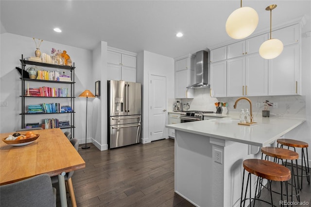 kitchen with stainless steel appliances, sink, wall chimney range hood, white cabinets, and hanging light fixtures