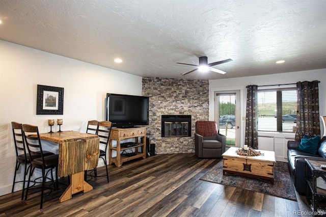 living room featuring ceiling fan, a fireplace, dark hardwood / wood-style floors, and a textured ceiling