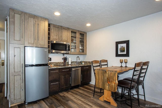 kitchen with appliances with stainless steel finishes, dark hardwood / wood-style floors, sink, light stone counters, and a textured ceiling