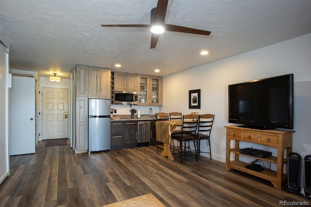 kitchen with appliances with stainless steel finishes, dark hardwood / wood-style floors, a kitchen breakfast bar, ceiling fan, and a textured ceiling