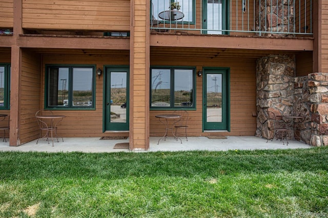 property entrance featuring a balcony, a patio area, and a lawn