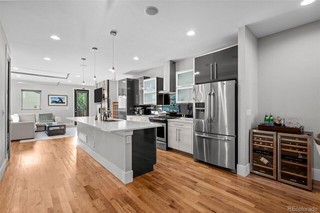 2523 N Humboldt St, Denver, CO 80205 - kitchen with appliances with stainless steel finishes, wall chimney exhaust hood, light countertops, light wood-type flooring, and an island with sink