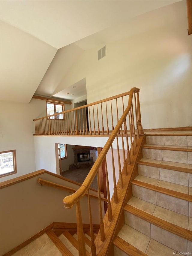 staircase featuring a brick fireplace, vaulted ceiling, visible vents, and tile patterned flooring