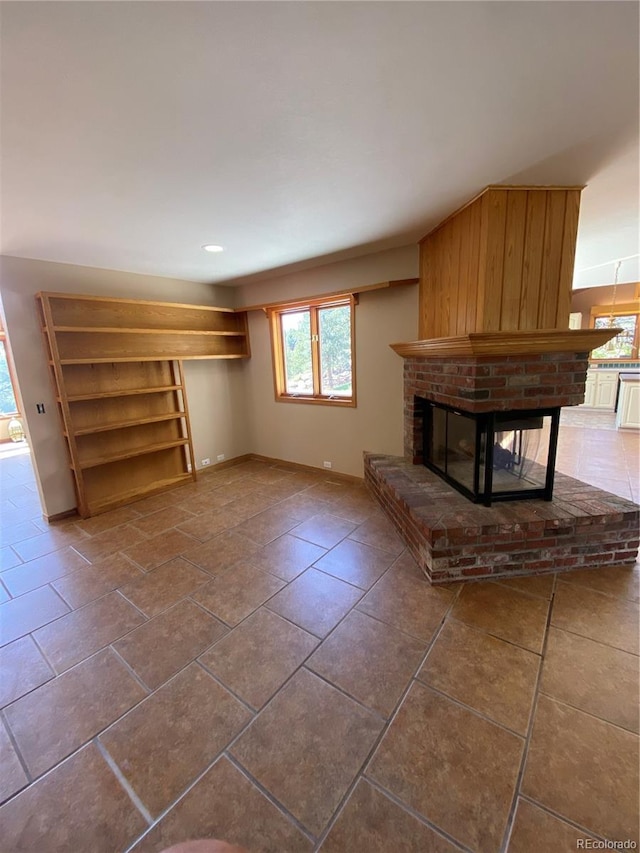unfurnished living room featuring a brick fireplace, baseboards, a wealth of natural light, and tile patterned floors