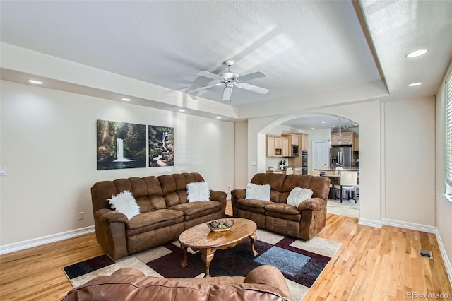 7482 Routt Ln, Arvada, CO 80005 - living area featuring arched walkways, light wood finished floors, a tray ceiling, a ceiling fan, and recessed lighting