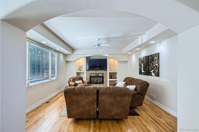7482 Routt Ln, Arvada, CO 80005 - living room with arched walkways, a ceiling fan, light wood-style flooring, a glass covered fireplace, and a raised ceiling