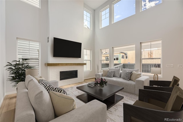 living room with a healthy amount of sunlight, a fireplace, a high ceiling, and light hardwood / wood-style flooring