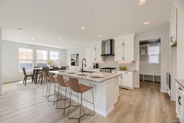 kitchen featuring stove, sink, wall chimney range hood, white cabinets, and an island with sink