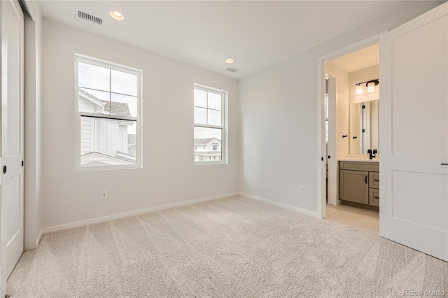 unfurnished bedroom featuring ensuite bathroom, a closet, and light colored carpet