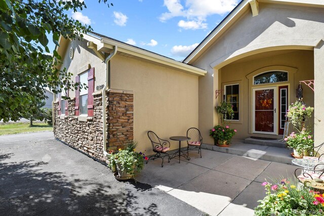 entrance to property with a patio area, stucco siding, and stone siding