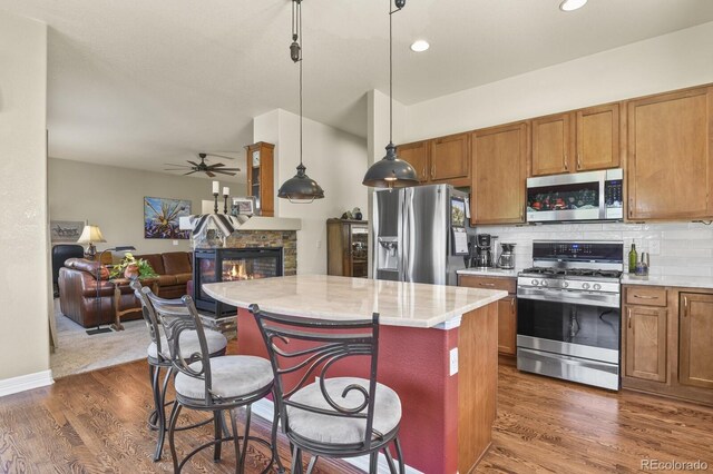kitchen with light countertops, appliances with stainless steel finishes, brown cabinetry, and a stone fireplace