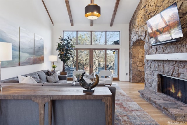 living room with beam ceiling, high vaulted ceiling, a stone fireplace, french doors, and light wood-type flooring