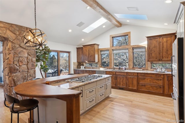 kitchen with sink, hanging light fixtures, a skylight, stainless steel appliances, and a center island