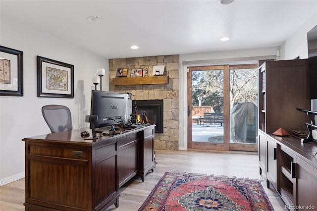 home office with a stone fireplace and light hardwood / wood-style flooring