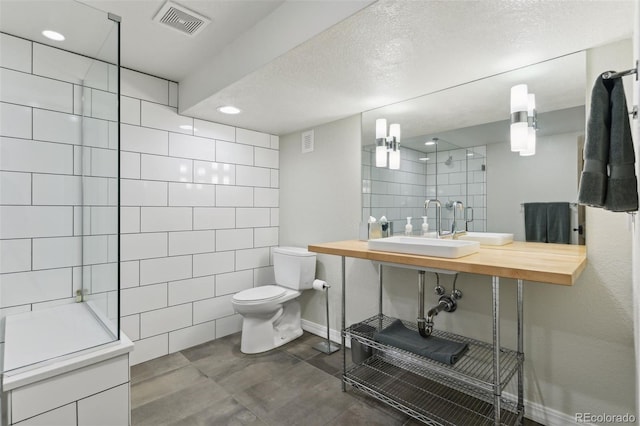 bathroom with sink, tile walls, a textured ceiling, a shower, and toilet