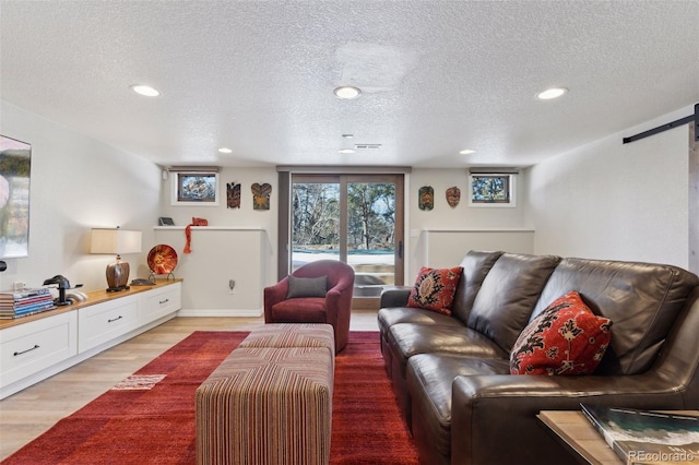 living room with a barn door, a textured ceiling, and light wood-type flooring