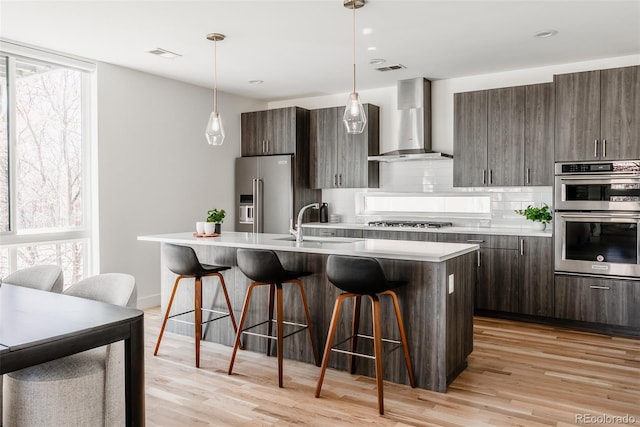 kitchen featuring appliances with stainless steel finishes, a sink, light countertops, wall chimney range hood, and backsplash