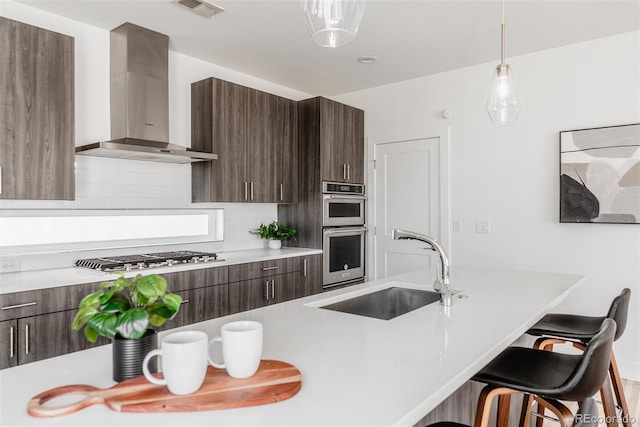 kitchen featuring dark brown cabinetry, stainless steel appliances, light countertops, wall chimney range hood, and a sink