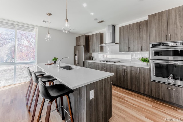 kitchen featuring decorative backsplash, wall chimney exhaust hood, a kitchen breakfast bar, stainless steel appliances, and a sink