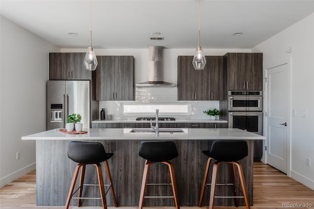 kitchen with wall chimney range hood, appliances with stainless steel finishes, light countertops, and a breakfast bar area