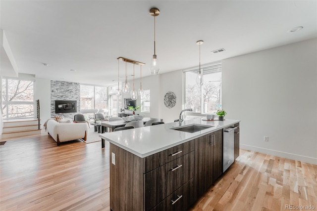 kitchen with a center island with sink, visible vents, a sink, a stone fireplace, and stainless steel dishwasher