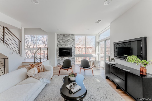 living room with plenty of natural light, a tiled fireplace, stairs, and light wood-style floors