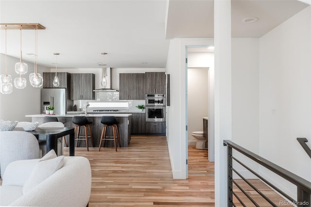 kitchen with a breakfast bar area, stainless steel appliances, light countertops, decorative backsplash, and wall chimney exhaust hood