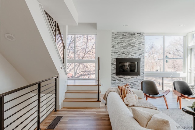 living room featuring stairs, a tiled fireplace, wood finished floors, and visible vents